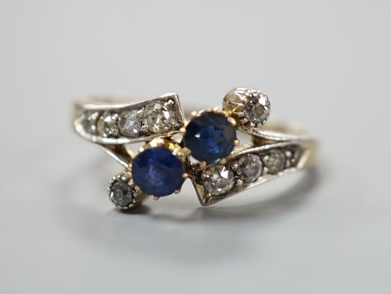 An 18ct, sapphire and diamond cluster set crossover ring, size S/T, gross 3.7 grams.